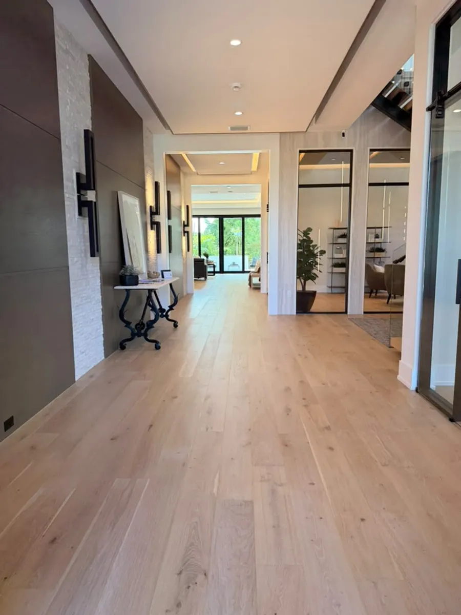 Wide hallway finished with light engineered wood flooring leading into an open great room