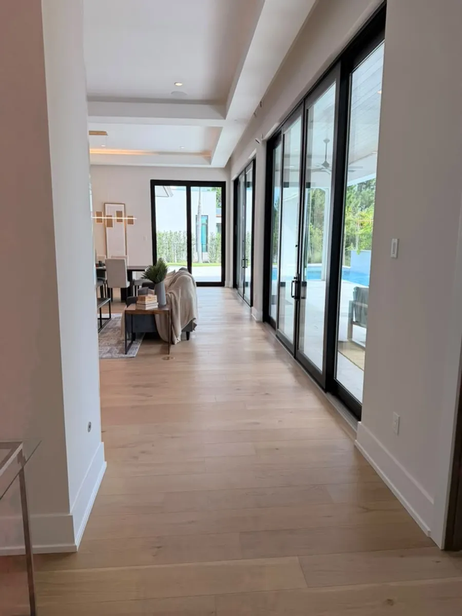Hallway finished with engineered wood flooring leading to glass doors and the pool patio