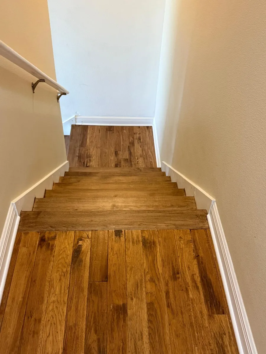Staircase with finished hardwood treads leading to a newly installed, unfinished hallway floor
